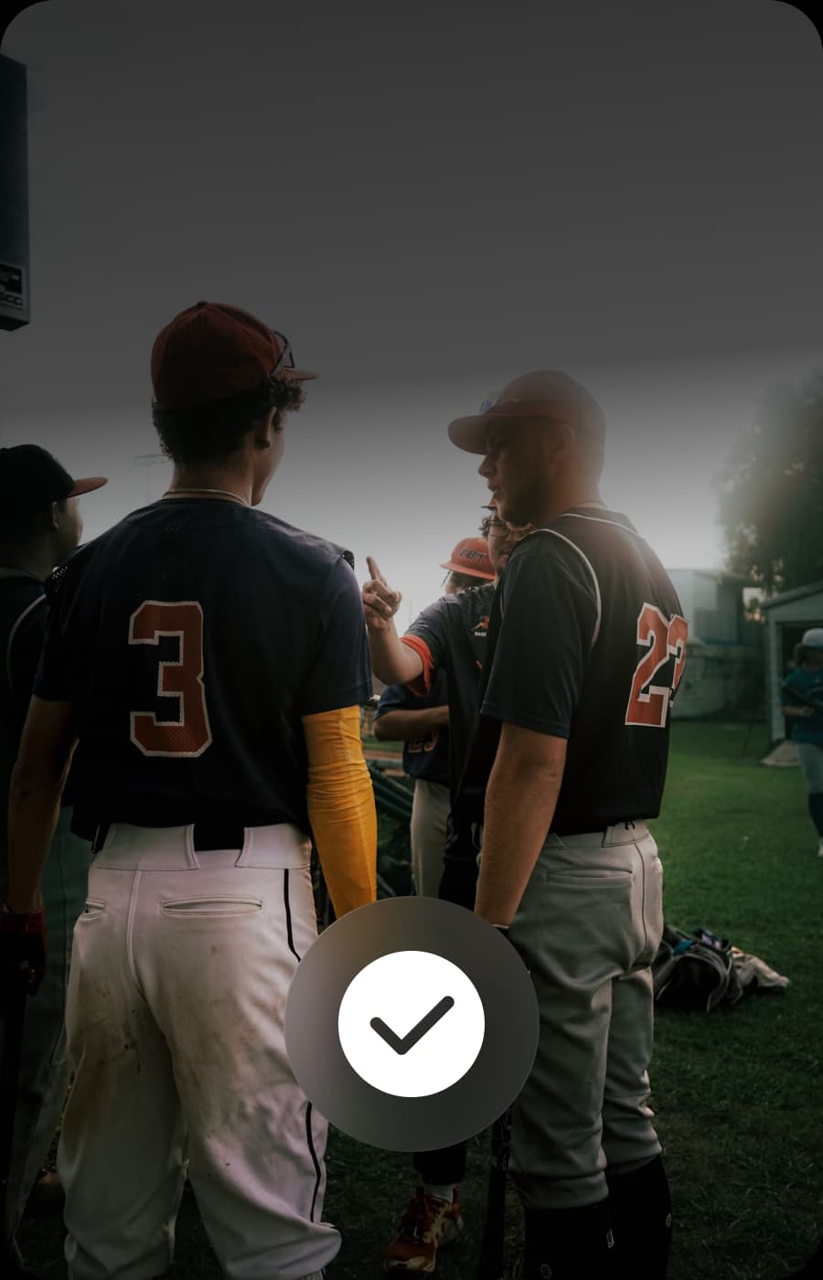 Two baseball players in uniform stand facing away from the camera, discussing something.