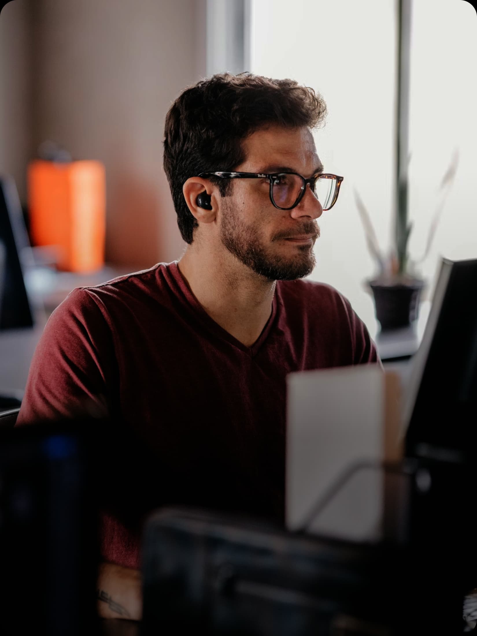 Man wearing glasses and a maroon shirt works at a computer in an office.