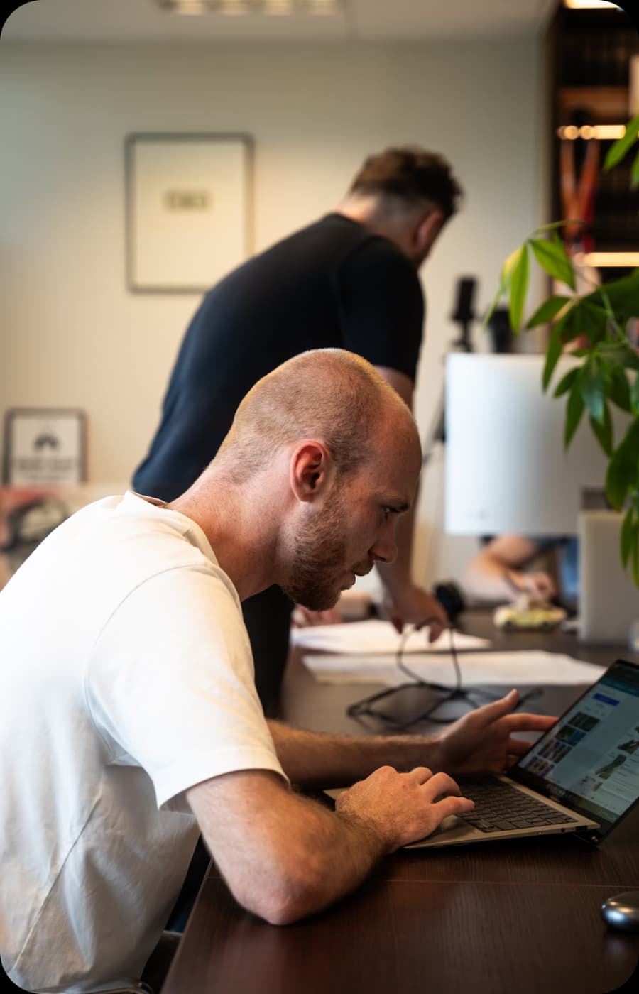 Two men collaborating at a desk with a laptop and papers.
